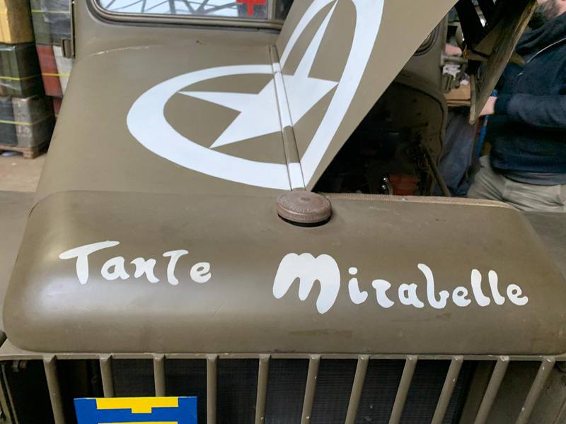 Gros plan sur le capot vert olive d'une ambulance, peint à la main : Tante Mirabelle.