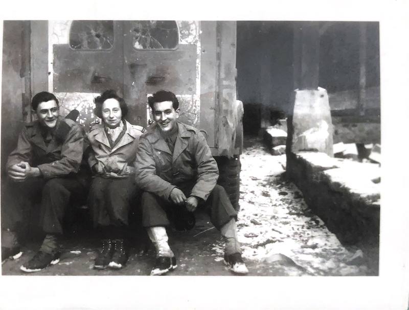 Deux soldats et Jacotte assis sur le marchepied arrière d'une ambulance abîmée, dans une rue enneigée.