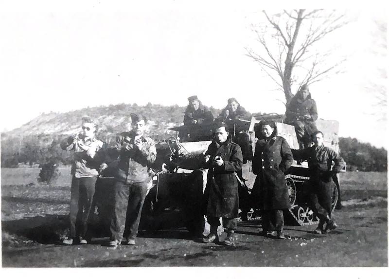 Un groupe de soldats et d'ambulancières en manteaux, debout devant un half-track, au pied d'une colline.