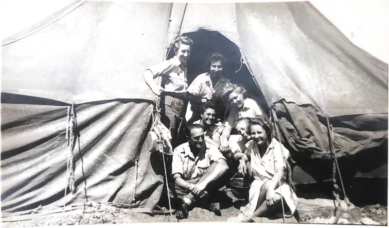Un groupe de jeunes femmes et un homme serrés à l'entrée d'une grande tente, souriants.